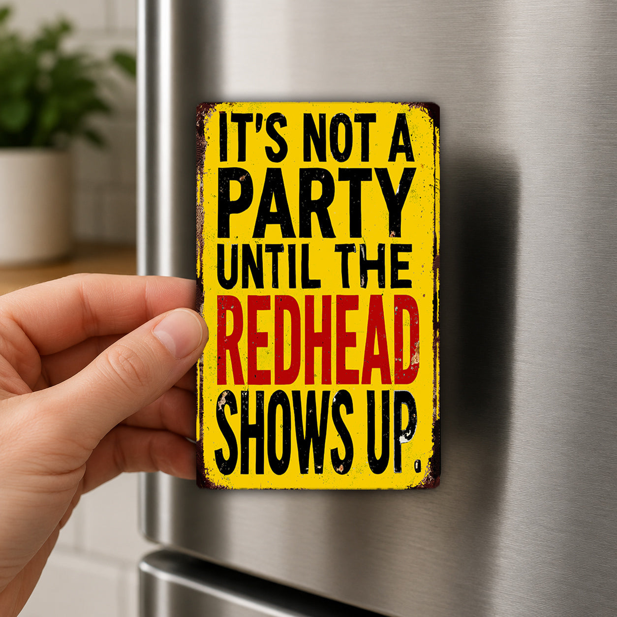 A person's hand holding a yellow sign with the text "It's not a party until the redhead shows up" on it.