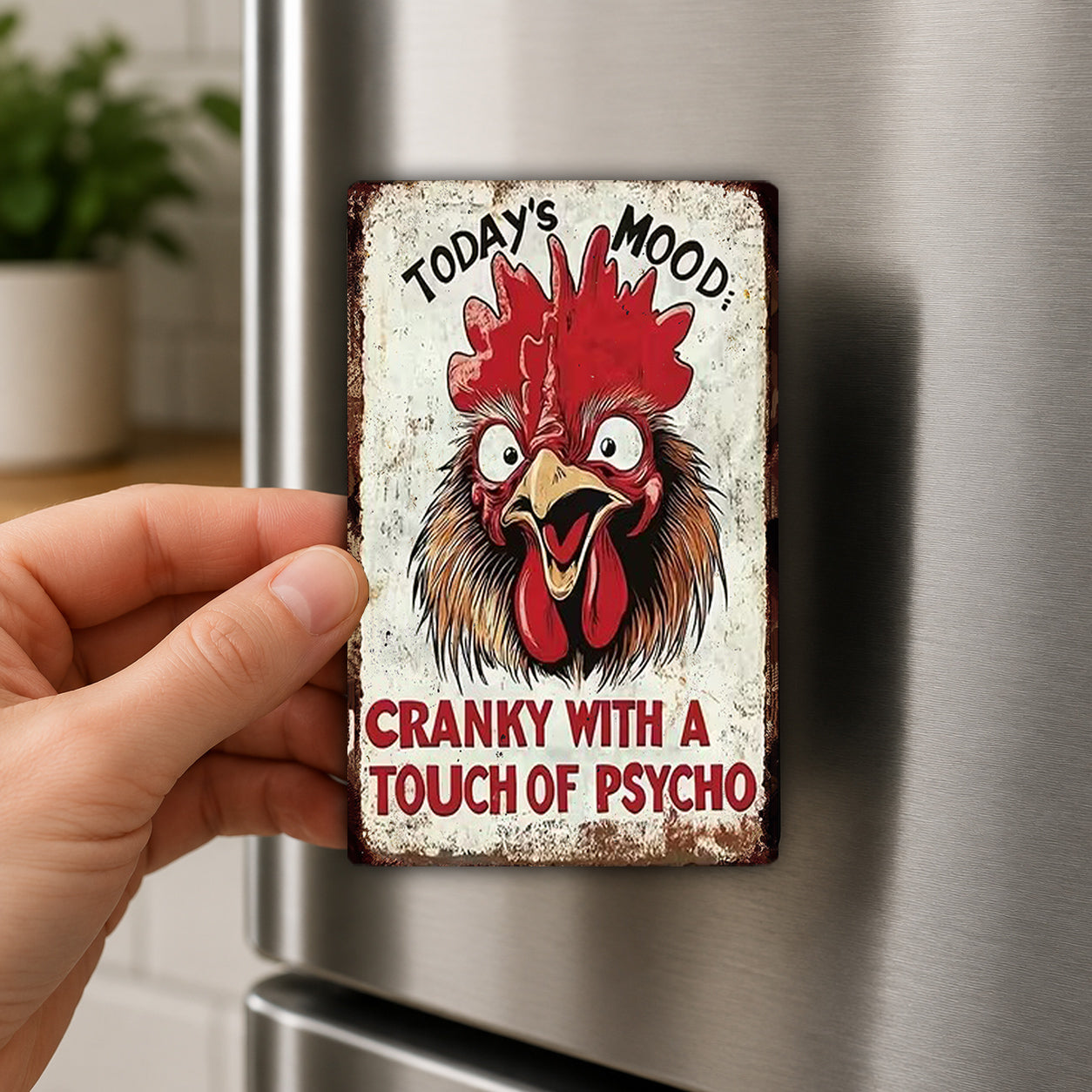 A person's hand holding a metal object with a humorous text and an illustration of a rooster's head on it.
