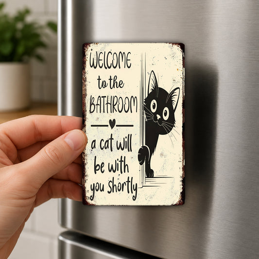 A person's hand holding a sign that says "Welcome to the Bathroom a cat will be with you shortly"