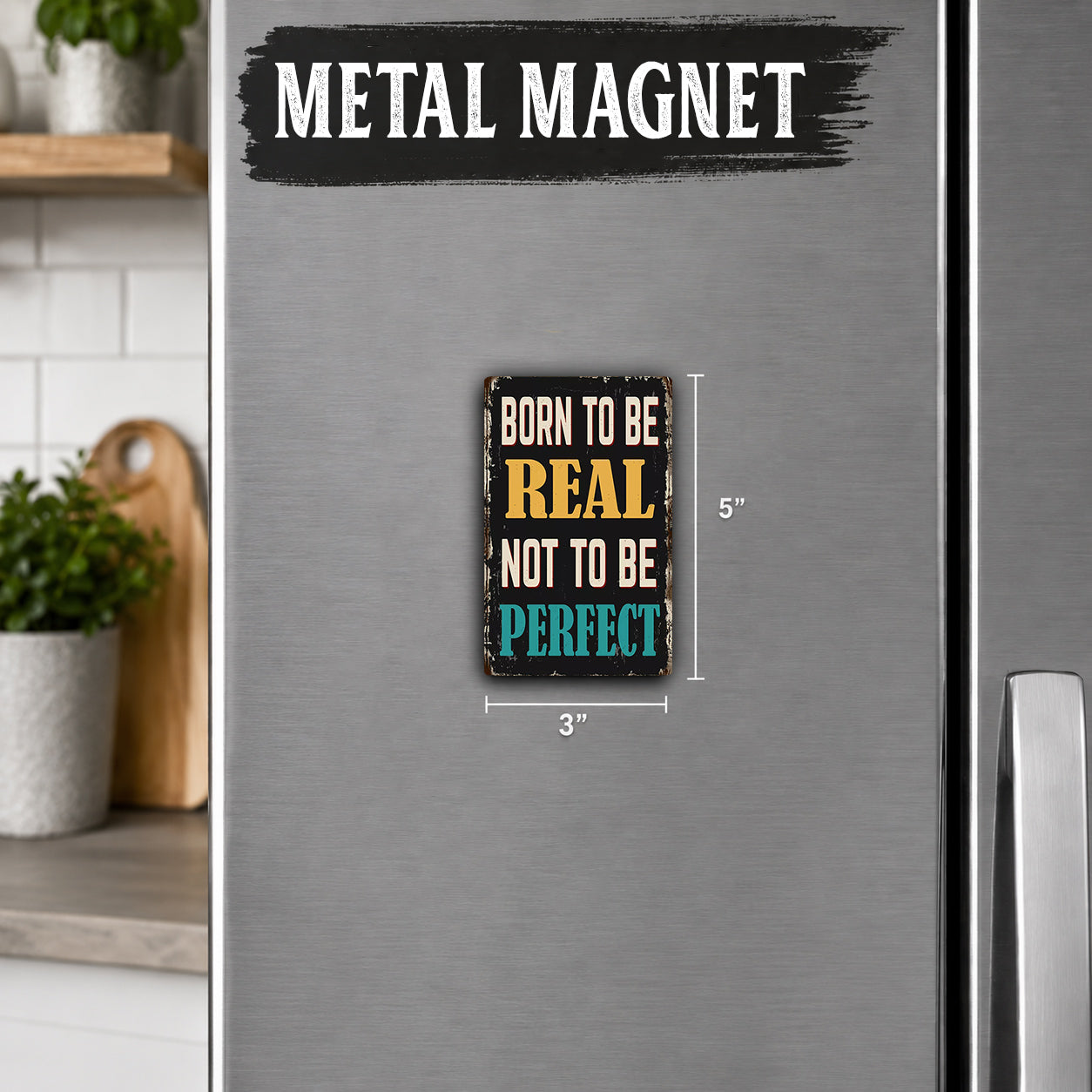 a small, colorful magnet with the text "Born to be REAL not to be PERFECT" on it, placed on a refrigerator.