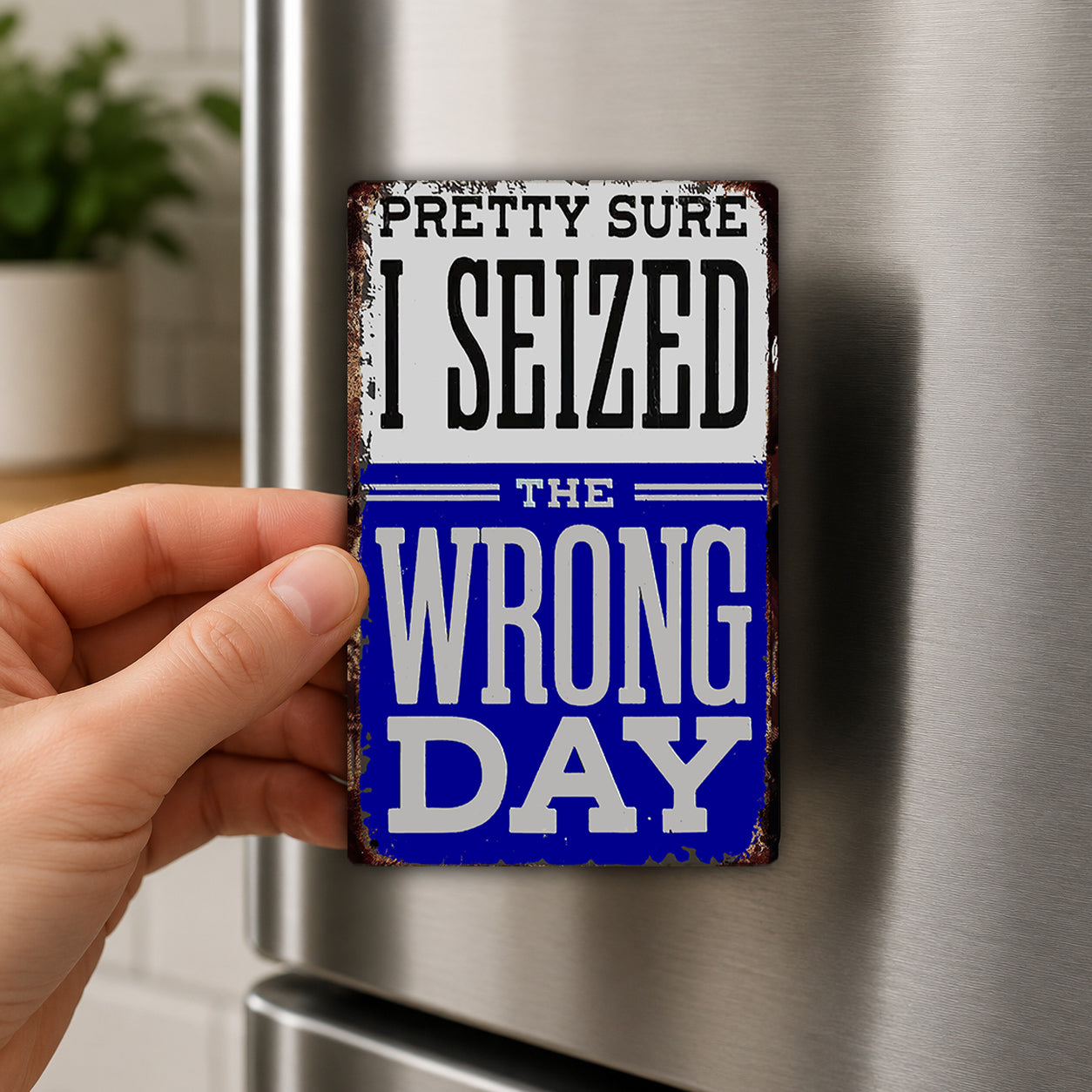 A person's hand is holding a metal refrigerator magnet with the text "PRETTY SURE I SEIZED THE WRONG DAY" on it.