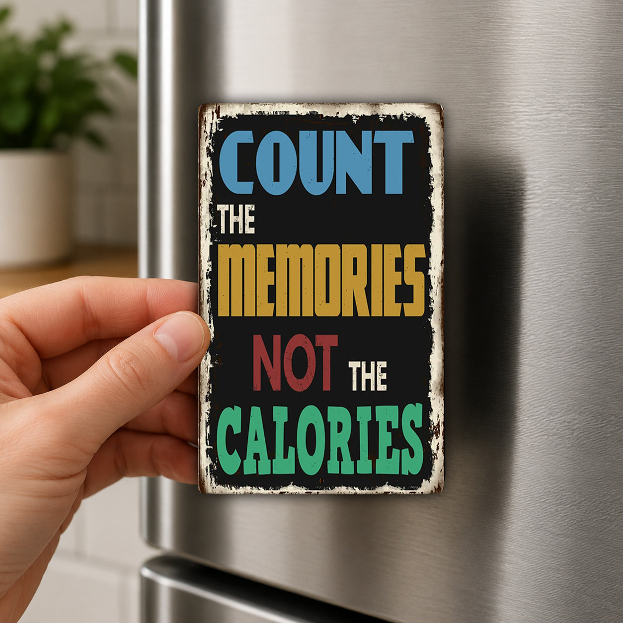 A person's hand holding a metal sign with the text "COUNT THE MEMORIES NOT THE CALORIES" on it.