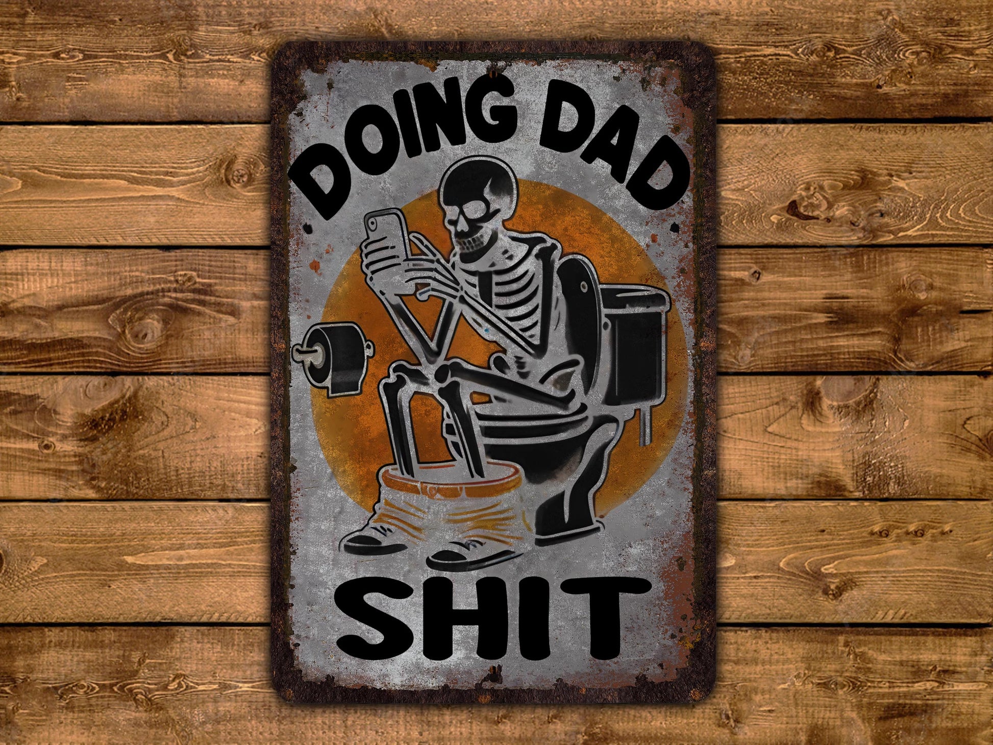 A metal sign with a skeleton sitting on a toilet and holding a phone, with the text "DOING DAD SHIT" written above it.