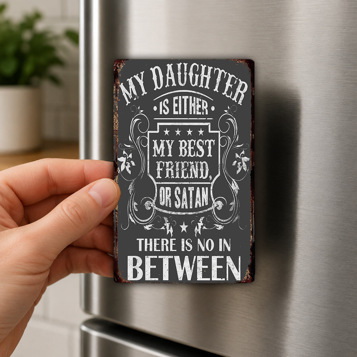 a person's hand holding a small, vintage-style sign with a message about the relationship between a daughter and a best friend or a friend and a devil.