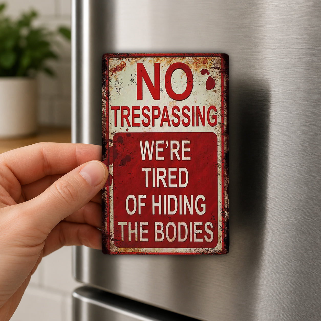 A person's hand is holding a metal sign with the text "NO TRESPASSING WE'RE TIRED OF HIDING THE BODIES" on it.