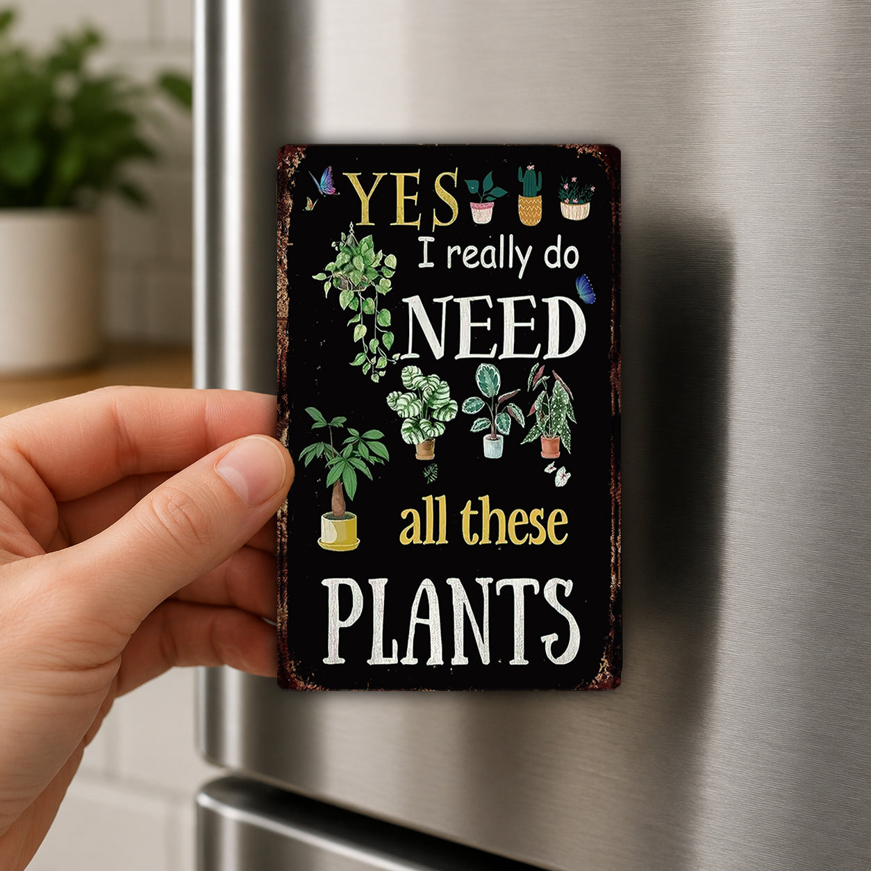 A person's hand is holding a small, decorative magnet with a message about plants.