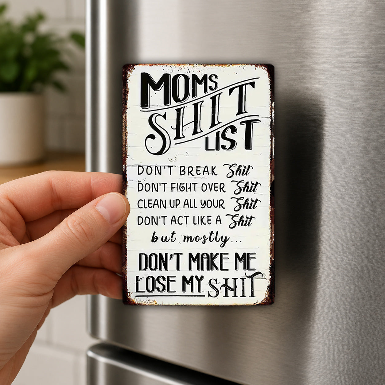 a person's hand holding a metal sign with a humorous message about a mother's "shitty list".