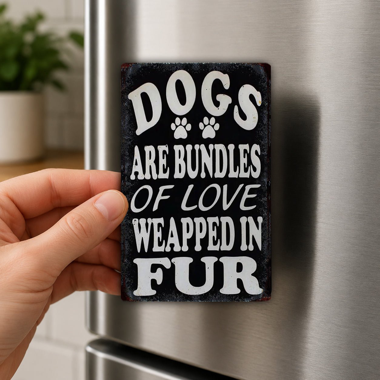 A hand is holding a sign that says "Dogs are bundles of love wrapped in fur" against a stainless steel refrigerator.