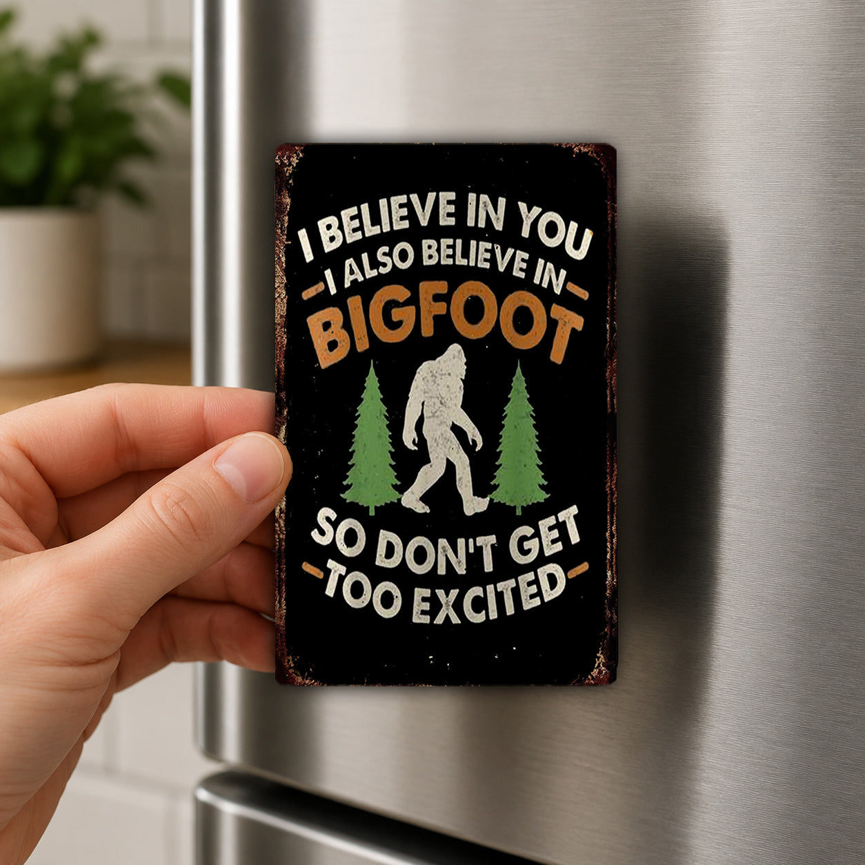A person's hand is holding a metal sign with a humorous text and a silhouette of a Sasquatch.