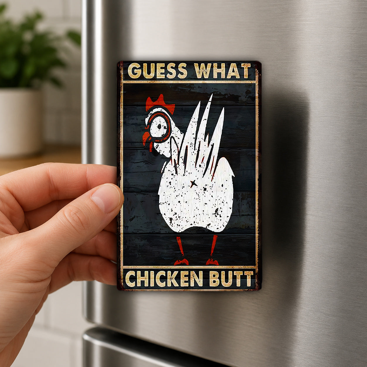 A person's hand is holding a metal refrigerator magnet with a humorous text and a cartoon image of a chicken.