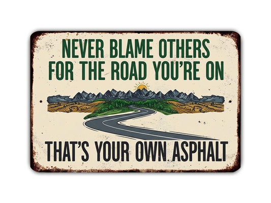 The image is a sign with a road leading to mountains, and it contains a message that says "Never Blame Others for the Road You're On. That's Your Own Asphalt."