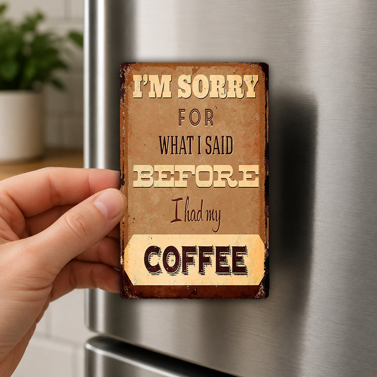 A hand holding a small, vintage-style magnet with the text "I'm sorry for what I said before I had my coffee" on it.